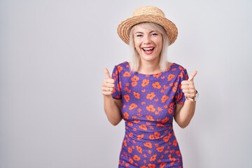 Young caucasian woman wearing flowers dress and summer hat success sign doing positive gesture with hand, thumbs up smiling and happy. cheerful expression and winner gesture.