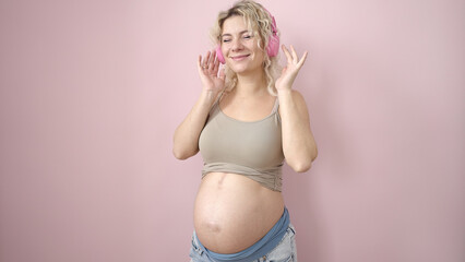 Fototapeta na wymiar Young pregnant woman smiling confident listening to music over isolated pink background