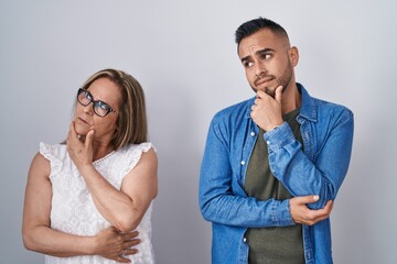 Hispanic mother and son standing together thinking worried about a question, concerned and nervous with hand on chin