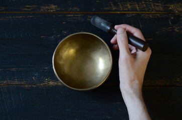 Tibetan singing bowl and hand with stick on the dark background - music instrument for meditation, relaxation, yoga practice, healing massage, chakra balance