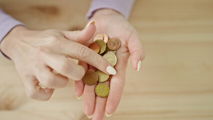 Young beautiful hispanic woman holding coins in the hand over wooden surface