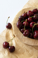 Cherries in a wooden bowl on brown textured paper on a white table