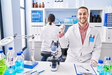 Young man working at scientist laboratory screaming proud, celebrating victory and success very excited with raised arm