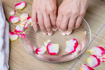 Obraz na płótnie Canvas Women's hands and a bowl of water for spa treatments with rose petals, close-up