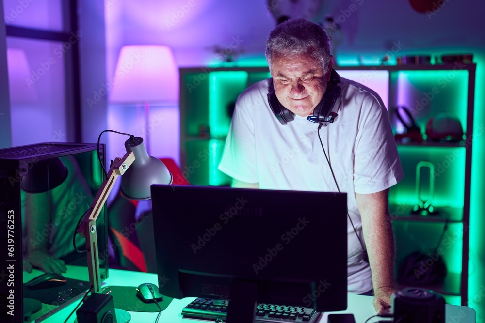 Poster middle age grey-haired man streamer smiling confident standing at gaming room