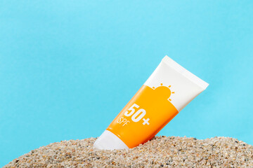 Sunscreen in an orange tube on blue background with beach sand, copy space. Summer beach, vacation concept, spf uv-protect cosmetics