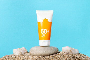 Sunscreen in an orange tube on blue background with beach sand, copy space. Summer beach, vacation...