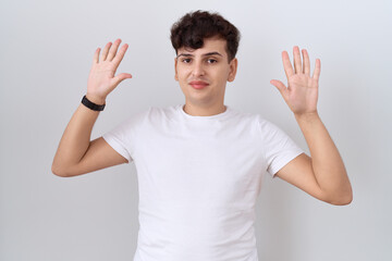 Young non binary man wearing casual white t shirt showing and pointing up with fingers number ten while smiling confident and happy.