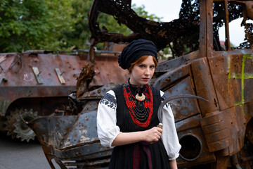 А woman in Ukrainian national embroidered dress vyshyvanka near destroyed russian tank and cars. - 619777801
