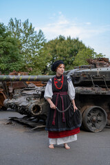 А woman in Ukrainian national embroidered dress vyshyvanka near destroyed russian tank and cars.