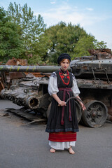 А woman in Ukrainian national embroidered dress vyshyvanka near destroyed russian tank and cars. - 619777846
