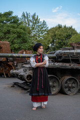 А woman in Ukrainian national embroidered dress vyshyvanka near destroyed russian tank and cars.
