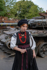А woman in Ukrainian national embroidered dress vyshyvanka near destroyed russian tank and cars. - 619777891