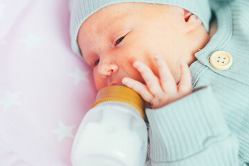 A newborn baby independently drinks milk or a formula milk from a bottle, at home