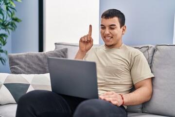 Young arab man using laptop at home smiling with an idea or question pointing finger with happy face, number one
