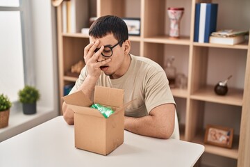 Young arab man with open gift in cardboard box peeking in shock covering face and eyes with hand,...