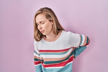 Obraz premium Young blonde woman standing over pink background suffering of backache, touching back with hand, muscular pain