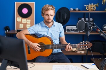 Caucasian man playing classic guitar at music studio skeptic and nervous, frowning upset because of problem. negative person.