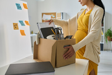Young pregnant businesswoman packing her things in box, she going on maternity leave