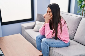 Young hispanic woman stressed sitting on sofa at home