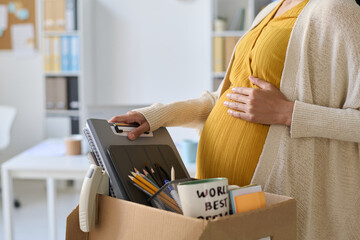 Close-up of pregnant busnesswoman packing her things in box before leaving her workplace in office