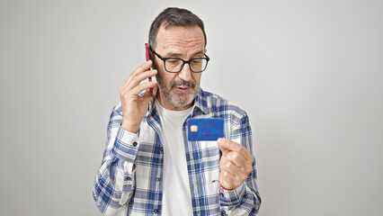 Middle age man talking on smartphone holding credit card over isolated white background