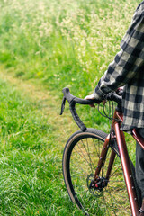 Naklejka premium A man holds a bicycle handlebar and walks in the forest, close-up.