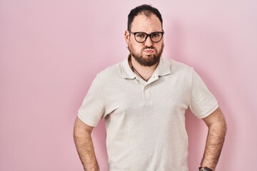 Plus size hispanic man with beard standing over pink background puffing cheeks with funny face....