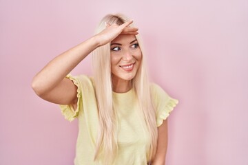 Fototapeta premium Caucasian woman standing over pink background very happy and smiling looking far away with hand over head. searching concept.