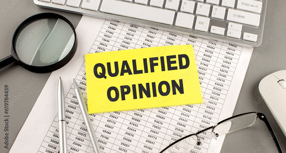Poster qualified opinion text written on a sticky on chart with keyboard and magnifier