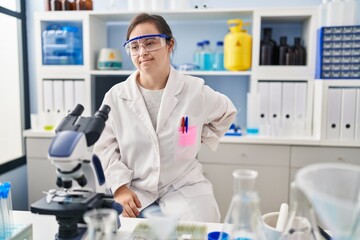 Hispanic girl with down syndrome working at scientist laboratory suffering of backache, touching back with hand, muscular pain
