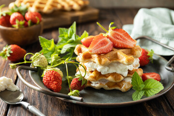 Homemade Belgian waffles with fresh berrie strawberries and ricotta cheese for breakfast on a rustic table.