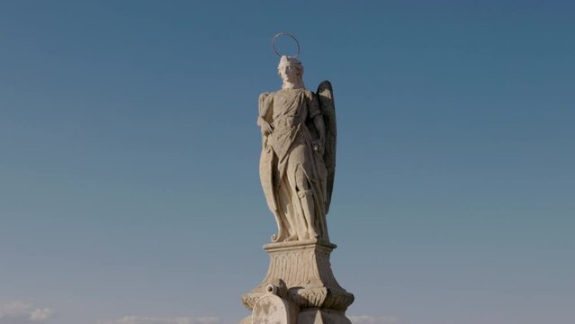 a close tilt up shot of the 17th century statue of the archangel raphael on the ancient roman bridge of cordoba, spain