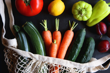 Mesh bag with fresh seasonal fruit and vegetable. Top view, dark background.