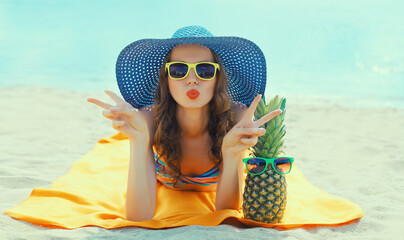 Summer vacation, happy young woman with pineapple fruits in straw hat lying on sand on the beach on...