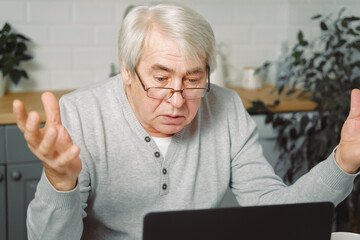 Old man outraged sitting at Laptop. Pensive Mature Grey hair 60s 70s Man waving hands. Thoughtful...