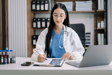 Female medicine doctor, physician or practitioner in lab room writing on blank notebook and work on laptop computer with medical stethoscope on the desk at hospital. Medic tech concept.