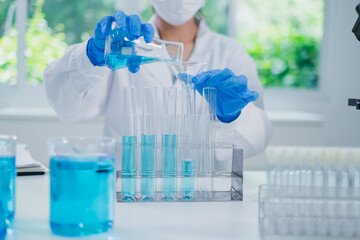 Female scientist or researcher is pouring blue substance or liquid in to a sample test tube. Concept of science, biochemistry, chemical, biotechnology laboratory. Substance study analyzing experiment