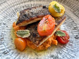 Two seabass fillets with tomatoes on a bed of red lentils puree on a rustic ceramic plate. Healthy...
