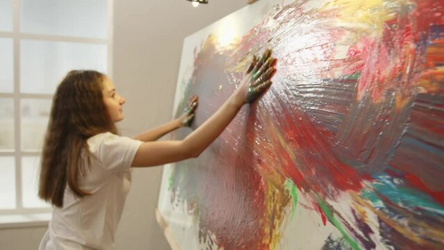 Girl 12 years old and child 4 years old draw picture with their hands in room using finger paints.