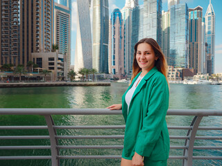 Fototapeta na wymiar young woman in green suit walks streets of Dubai, Dubai Marina district. United Arab Emirates trip concept. the idea of successful expat, moving to another country, work visa