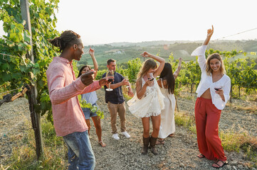 Multiracial friends dancing at summer party inside vineyards - Happy people having fun together drinking red wine  at coutryside resort - Travel, celebration and tasting event concept - Focus on faces