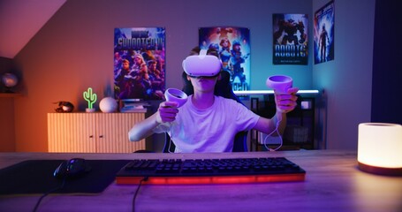 Young gamer in VR headset plays virtual reality online video game using wireless controllers. Boy having fun in leisure time in stylish neon room. Gaming at home. View from PC screen perspective. © Framestock
