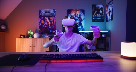 Young gamer in VR headset plays virtual reality online video game using wireless controllers. Boy...