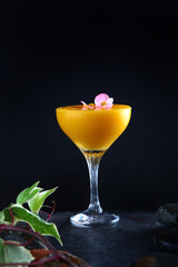 Alcoholic cocktail based on mango pulp. Delicious mango cocktails. The cocktail is decorated with a pink flower.Vertical photo.Space for copying. Black background.