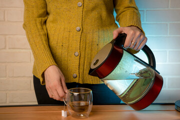 woman pouring hot water from a kettle into a clear glass mug