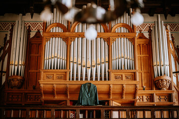 The dark brown organ in the church sets a solemn tone, while the groom's suit is carefully hung beneath it, waiting for the special moment.