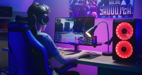 Young gamer in headphones plays in first person shooter on computer. Online video game live...
