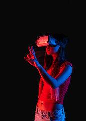 Side view of young unrecognizable chinese woman standing touching air and wearing virtual reality headset on colorful red studio background