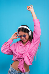 Cheerful asian female with eyes closed in earphones enjoying favorite song and smiling while dancing against blue background
